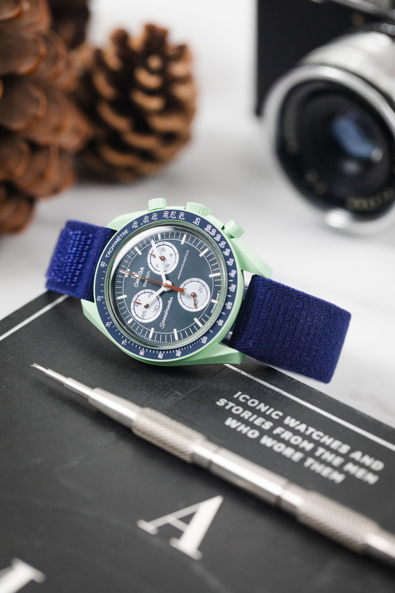 OMEGA x Swatch Mission on Earth watch on a HIRSCH Vocem Blue strap, lying on a book with a spring bar tool.
