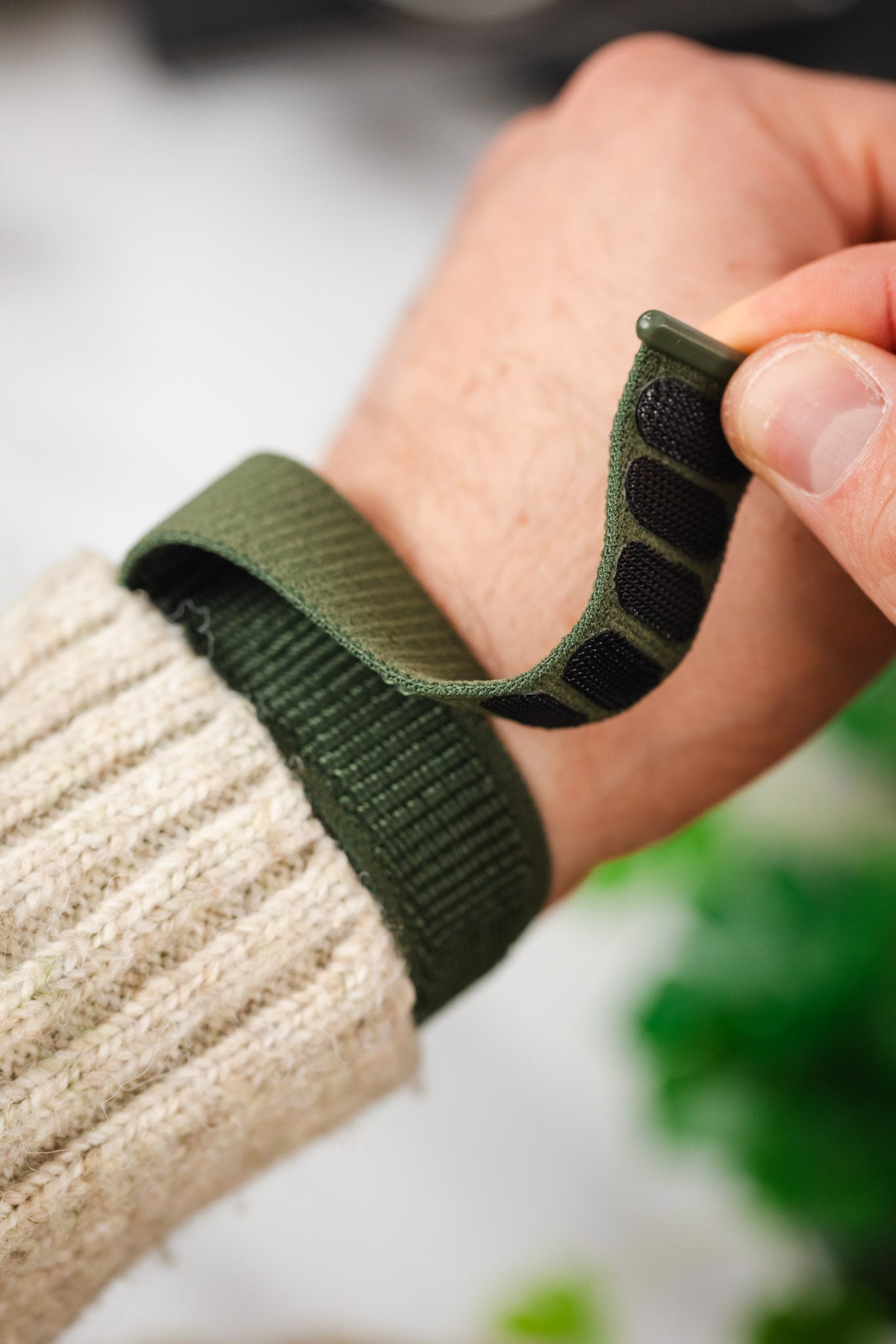 Hand securing the adjustable hook-and-loop fastener of the HIRSCH Vocem Green textile watch strap on a wrist.