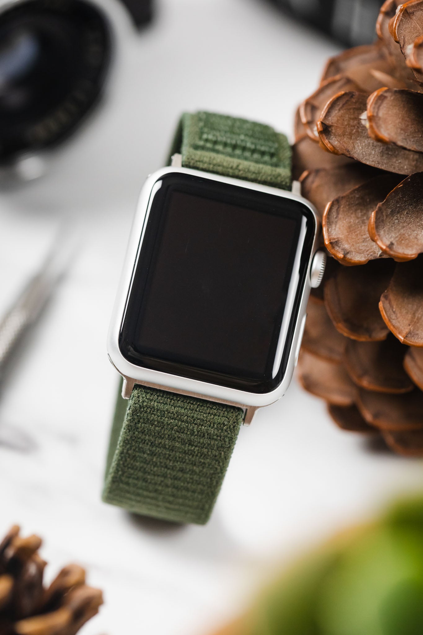 Close-up of an Apple Watch on a HIRSCH Vocem Green strap, styled with natural pinecones and accessories.