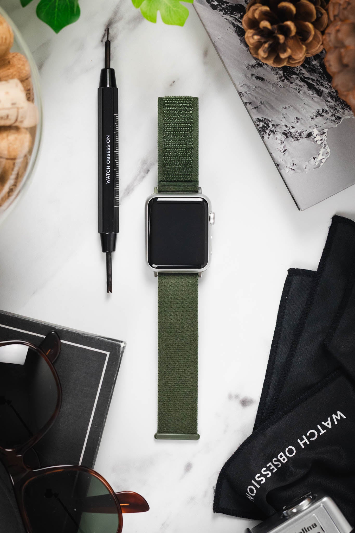 Flat lay of an Apple Watch on a HIRSCH Vocem Green strap, displayed with a spring bar tool and other gear.