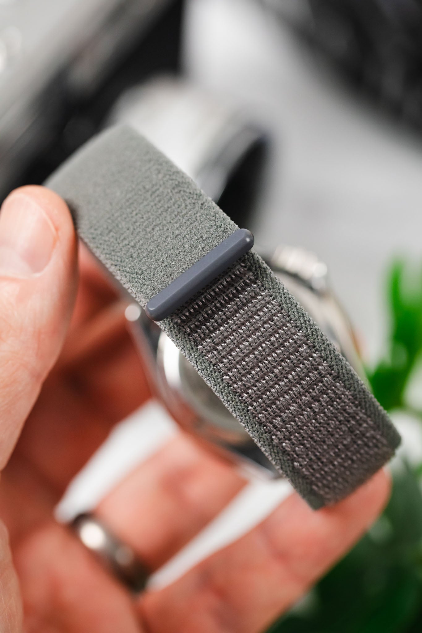 Hand holding a HIRSCH Vocem Grey sporty textile watch strap with a flexible grey loop and woven texture.