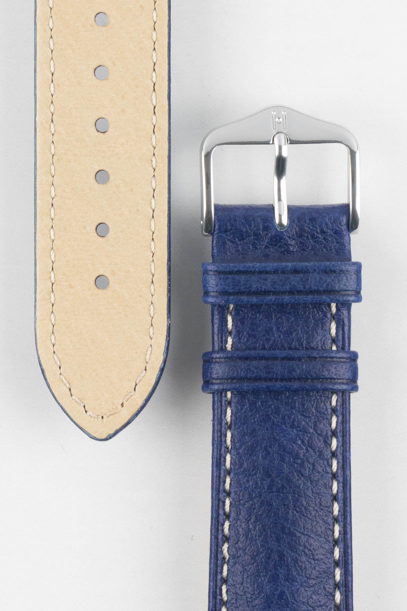 Close-up showing the beige "Hirsch Artisan Leather" lining of a strap alongside the top blue leather section with a silver pin buckle.