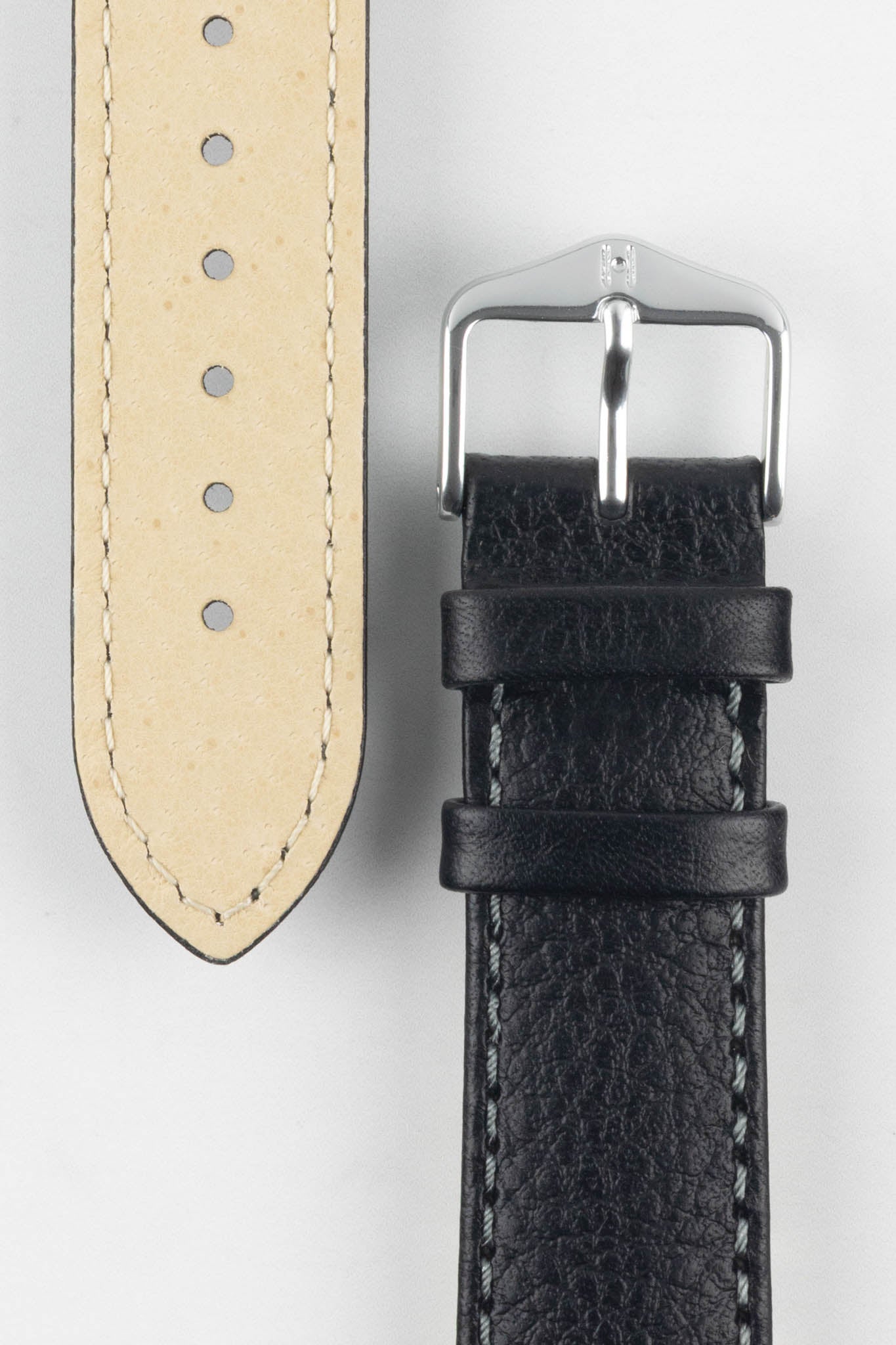 Close-up of a black watch strap showcasing its beige lining, grain texture, and classic silver buckle with a signature logo.