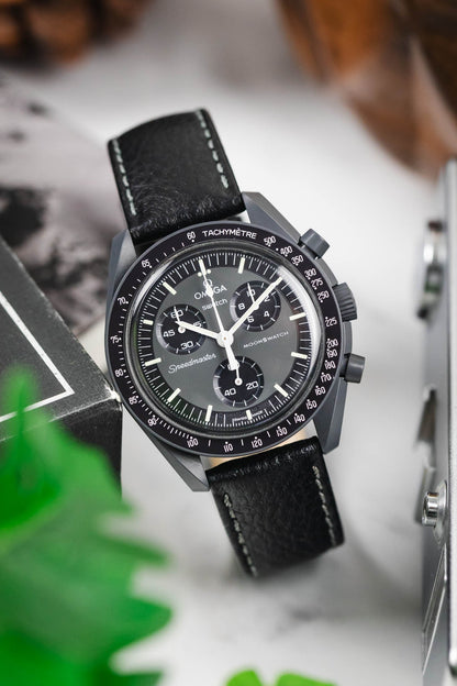 OMEGA x Swatch MoonSwatch Mission to the Moon watch on a black textured leather strap, white stitching, lifestyle shot.