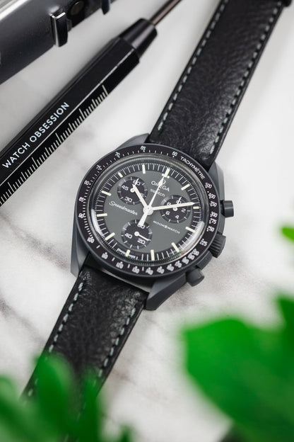 OMEGA x Swatch MoonSwatch with a black leather watch strap, white stitching, alongside a 'Watch Obsession' spring bar tool.