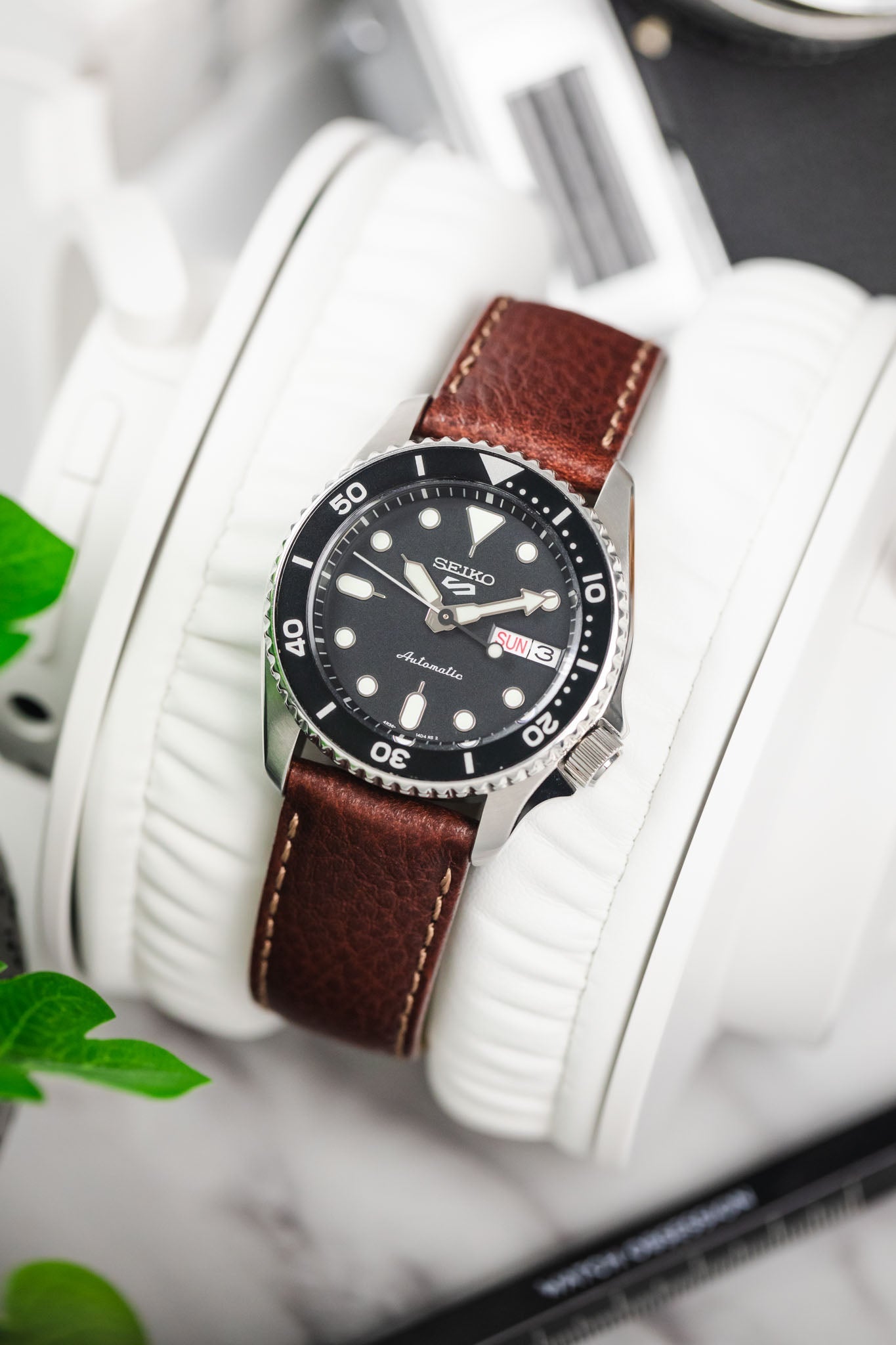 Seiko 5 Sports automatic diver on a brown leather watch strap with contrast stitching, resting on white headphones.