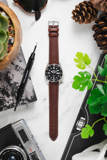 Flat lay of OMEGA x Swatch MoonSwatch on a black leather strap with tool and other accessories on a white surface.