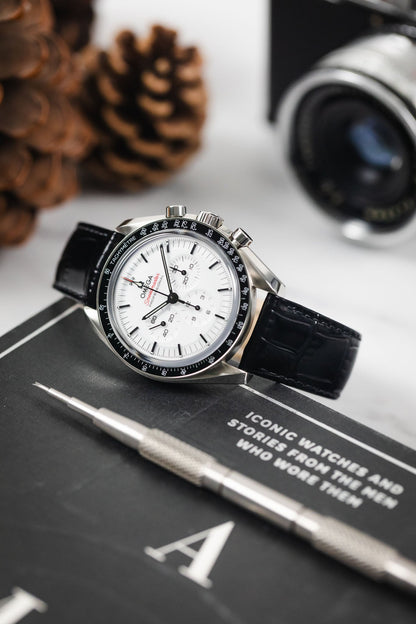 Omega Speedmaster automatic watch on a brilliant black Louisianalook strap, styled on a desk with accessories.