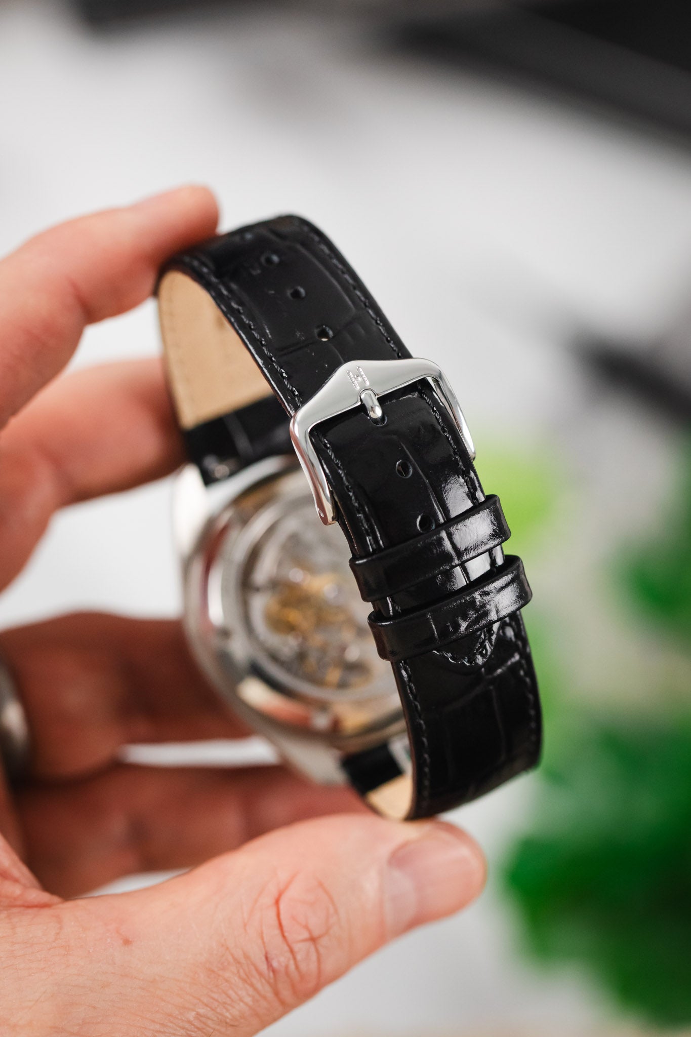 Close-up of an elegant black alligator-embossed watch strap with silver buckle.