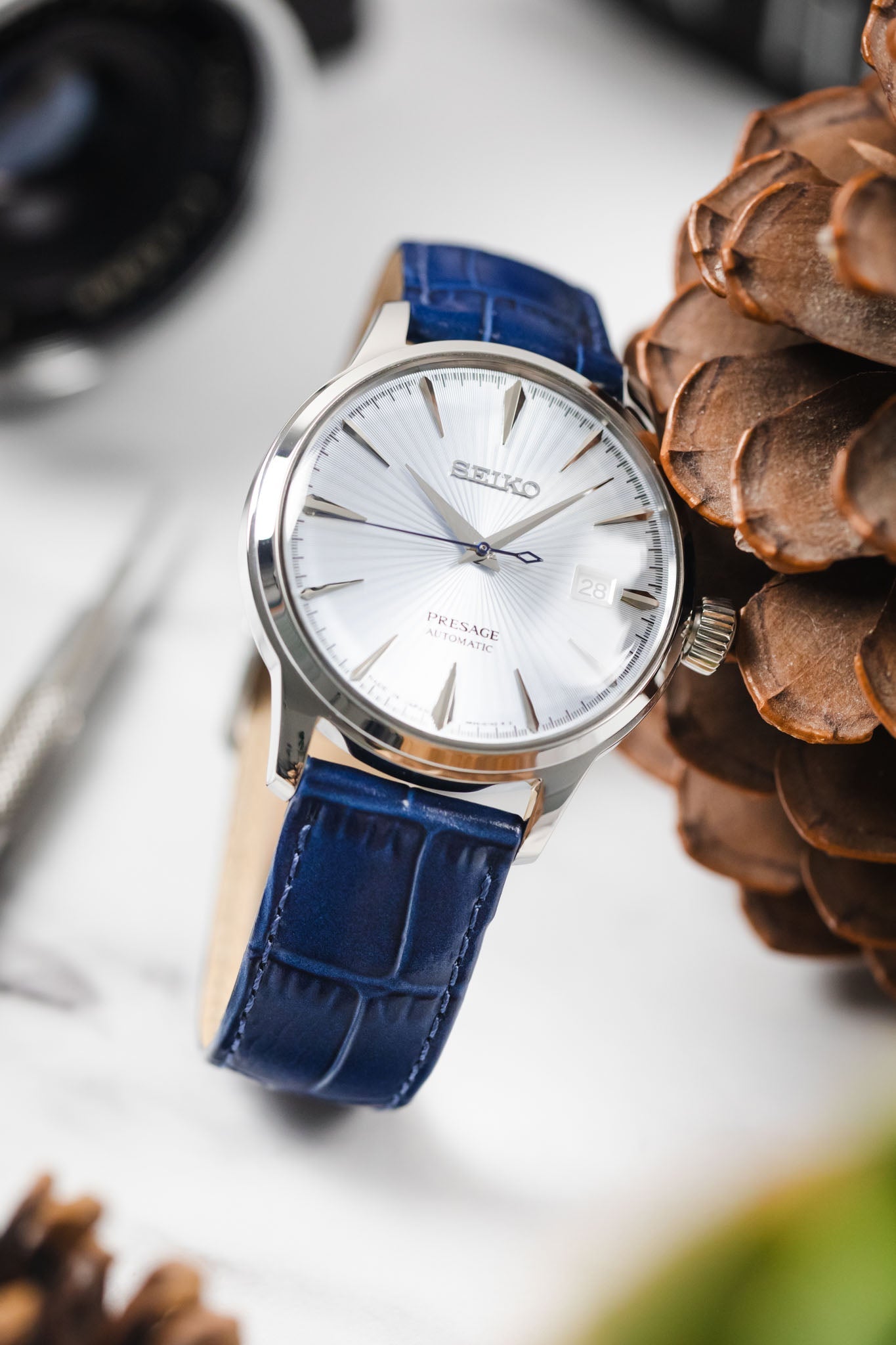 Seiko Presage automatic watch on a brilliant blue Louisianalook strap, resting next to large pinecones.