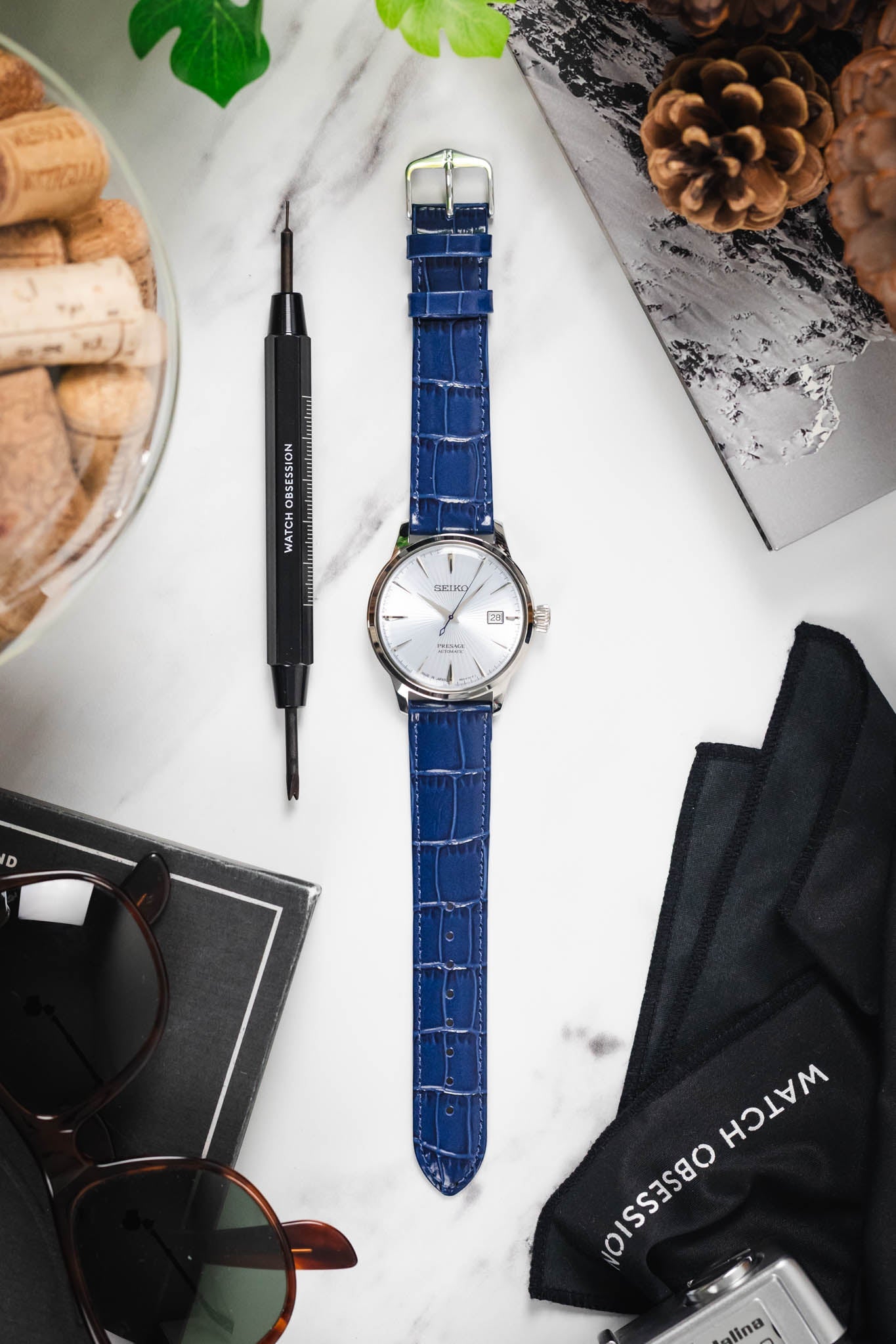 Flat lay of a Seiko Presage watch on a blue Louisianalook strap, styled with a spring bar tool and other gear.