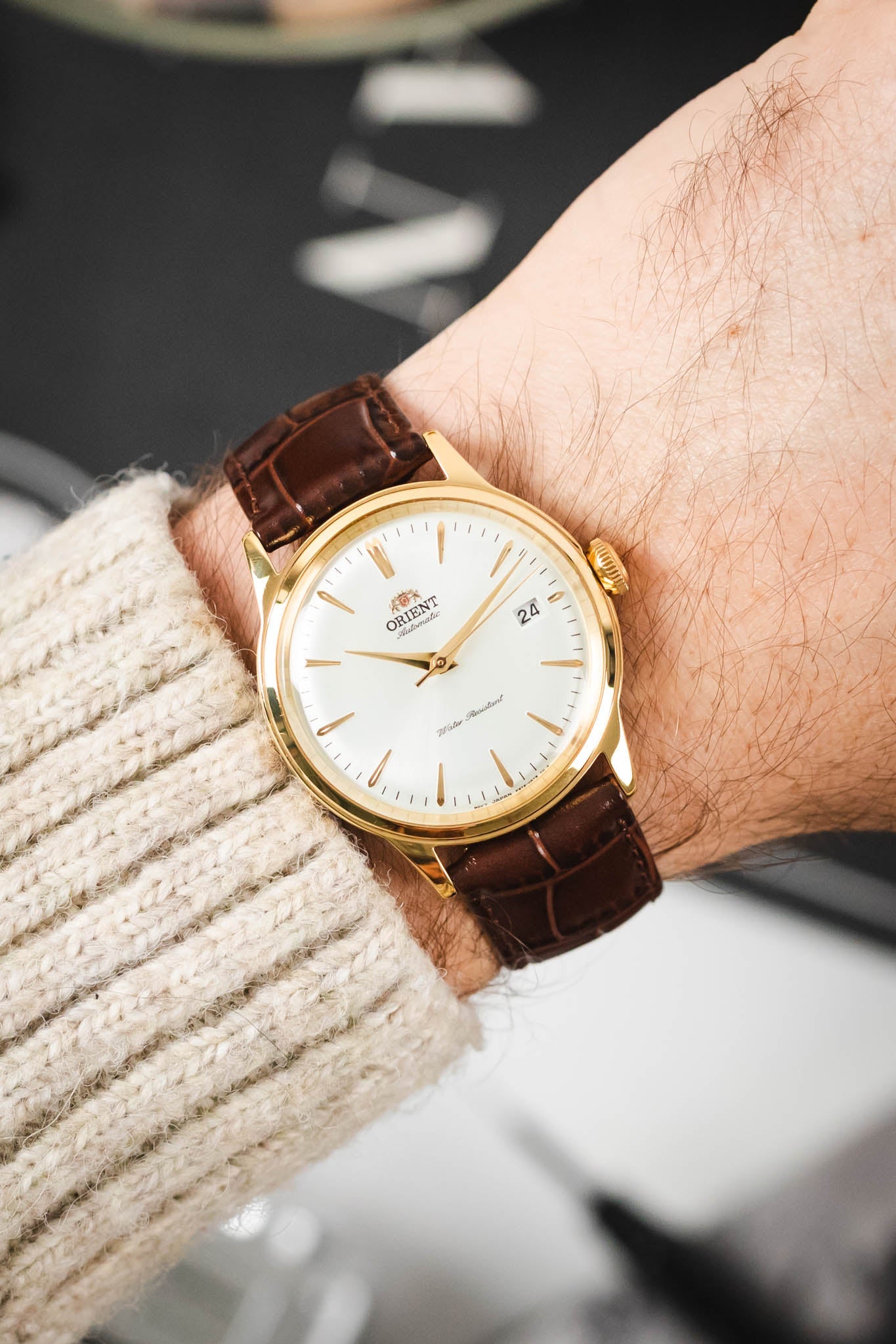 Gold-case Orient automatic watch on an embossed brown Louisianalook strap, worn on a wrist with a sweater.
