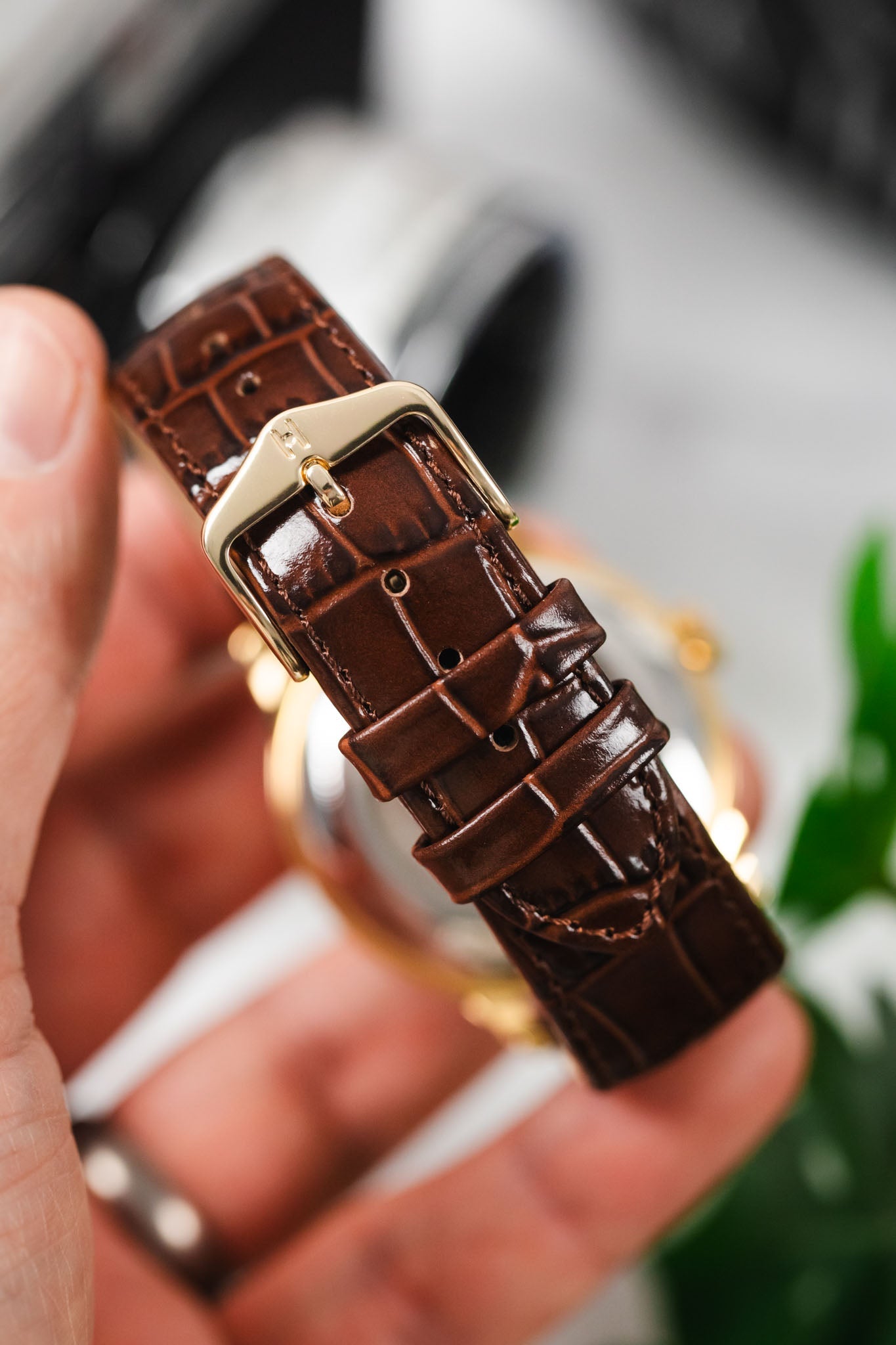 Hand holding a gold-case Orient watch with a close-up of the elegant brown alligator-embossed strap and gold buckle.